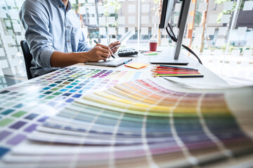 Image of male creative graphic designer working on color selection and drawing on graphics tablet at workplace with work tools and accessories in workspace