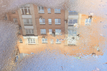 Poster - rain puddle with reflection of high-rise urban house on asphalt road in city on sunny autumn day