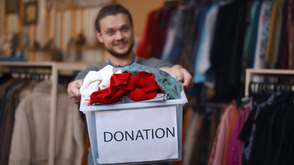 Smiling young man holding donation box, posing in modern charity shop