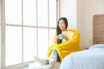 Poster - Beautiful young woman wrapped in warm plaid drinking tea near window