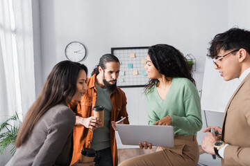 Wall Mural - Hispanic office workers looking at laptop in hands of female colleague during break at workplace