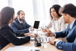 © LIGHTFIELD STUDIOS - Smiling hispanic businesswoman working with colleagues near laptop and water on blurred foreground on table