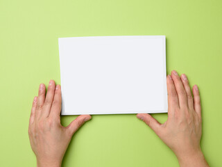 two female hands holding an empty white frame on a green background