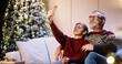 © VAKSMANV - Portrait of happy smiling Caucasian old grandpa with teen grandchild sitting in decorated room and taking selfie photos on smartphone at home near glowing new year tree. Christmas holidays concept