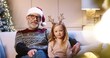 © VAKSMANV - Portrait of loving happy Caucasian senior grandpa in glasses wearing santa hat spending Christmas together with joyful grandchild sitting in decorated room near glowing xmas tree embracing together