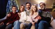© VAKSMANV - Close up of Caucasian cheerful family sitting together at cozy home near decorated glowing xmas tree smiling and looking at camera on Christmas Eve. New Year concept. Winter holiday celebration