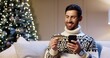 © VAKSMANV - Close up portrait of happy Caucasian handsome guy makes purchase on internet buying xmas gifts paying with credit card at home near glowing tree. Christmas gifts and presents. Holiday shopping concept