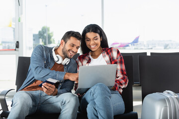 Wall Mural - happy interracial couple looking at laptop in airport