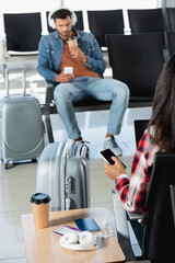 Wall Mural - back view of woman holding smartphone with blank screen near luggage and man on blurred background