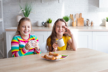 Portrait of two teenage beautiful smiling hipster girls in fashionable clothes. carefree children posing against the backdrop of the kitchen. Positive models have fun with sweets.