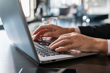 Office manager male hands typing on laptop keyboard, closeup. Businessman working with laptop, no face, male hands on black keyboard on wooden office table, concept of work