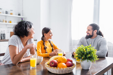 Wall Mural - Smiling hispanic family looking at each other during breakfast in kitchen