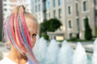 © Kirill Gorlov - Cute adorable caucasian little kid girl with multicolored pastel chalk pained dyed blond hair on city street with fountain background. Female child portrait pink colorful hairstyle smiling outdoors