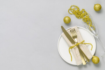 Festive table setting with white plate, golden cutlery, wine glass and gold xmas decorations on light gray tabletop. Christmas table setting. Flat lay, top view. Minimal style, copy space