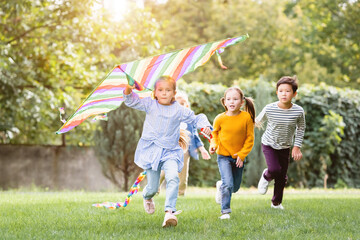 Girl holding flying kite while running near multiethnic friends in park