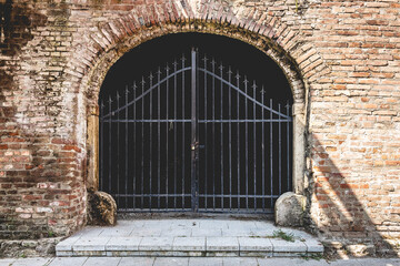 Poster - Closeup shot of a locked gate with an arch-shaped brick wall entrance