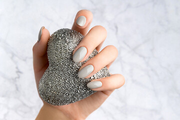 Beautiful womans hand with manicure holding silver heart