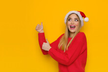 Happy Young Woman In Santa Hat Is Showing Thumbs Up And Talking