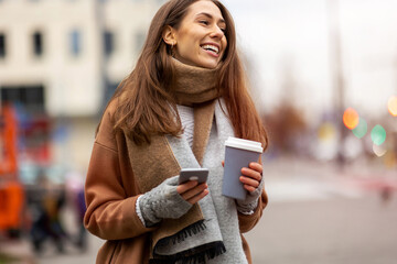 Wall Mural - smiling young woman with smart phone and coffee cup outdoors at urban setting