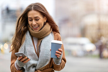 Wall Mural - smiling young woman with smart phone and coffee cup outdoors at urban setting