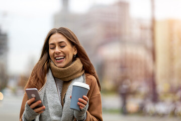 Wall Mural - smiling young woman with smart phone and coffee cup outdoors at urban setting