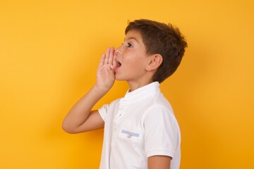 little cute Caucasian boy kid wearing white t-shirt against yellow wall profile view, looking happy and excited, shouting and calling to copy space.