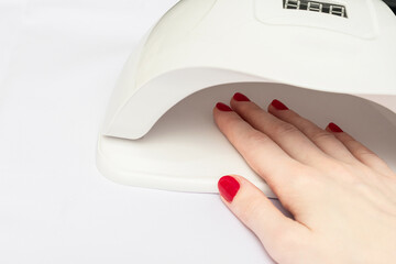 Female hand in UV lamp lights for red nails, close up, white background