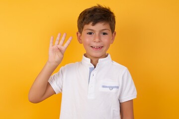 little cute Caucasian boy kid wearing white t-shirt against yellow wall showing and pointing up with fingers number four while smiling confident and happy.