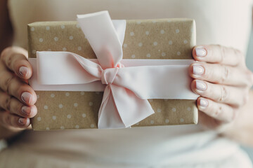 Wall Mural - Close-up of female hands holding a small gift wrapped with a satin ribbon