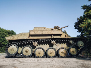 An old Soviet model of the T-70 tank stands against the background of trees and sky. Light armored military equipment of the USSR.