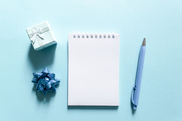 Notebook and pen on a blue background, spiral notepad with gift on a table. space for your text, greetings, top view.