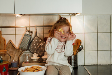 Wall Mural - Christmas. Adorable 3 year old girl eating Christmas cookies and drinking hot tea in New Year's decorations. Winter holidays.