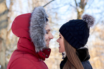 young couple in love, enjoying winter weather outside in park forest. brunette man in red jacket and