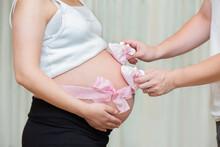 Cropped Hands Holding Baby Booties On Pregnant Woman Belly At Home