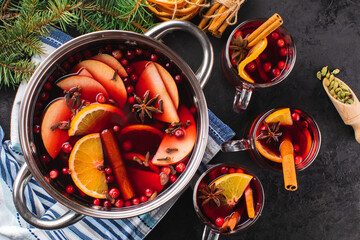 Wall Mural - Mulled wine or punch in a glass and hot wine in a cooking pot with spices and fruits on a black textured background, top view. Christmas hot drink.