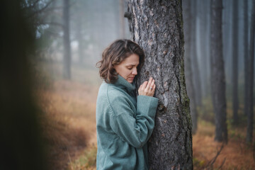 Wall Mural - Happy woman in warm cozy green sweater in a beautiful foggy pine forest