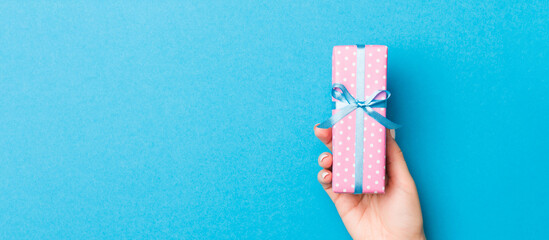 Wall Mural - Woman arms holding gift box with colored ribbon on blue table background, top view and copy space for you design