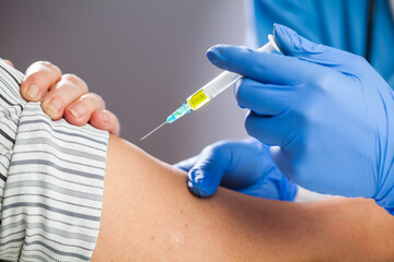 Coronavirus COVID-19 immunisation concept,medical worker wearing blue protective latex gloves holding syringe filled with yellow liquid,giving patient vaccine shot dose,caucasian hand closeup detail