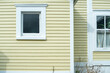 © Dolores  Harvey - A bright yellow lateral clapboard wooden exterior wall of a house or building with a small single glass and double hung window. The trim around the windows is white. There are shrubs below the window.
