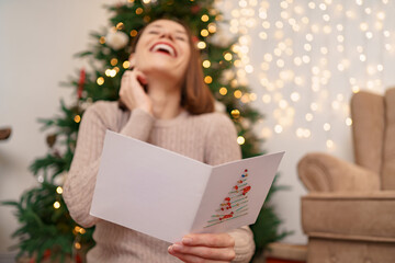 Beautiful woman laughing while reading a Christmas greeting card with light in background. Copy space for text.