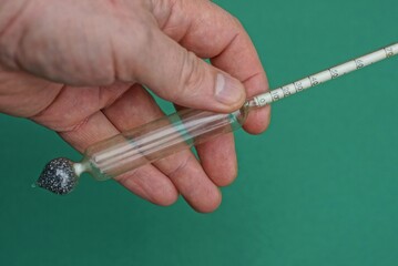 fingers holding an old glass alcohol thermometer on a green background