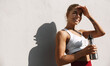 © Liubov Levytska - Shot of happy female runner standing outdoors holding water bottle and smiling. Fitness woman taking a break after workout