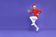 © NaMong Productions - Young asian man in red casual attire wearing Santa hat jumping with pointing finger aside front a copy space and smile face on purple background.Happy new year concept.