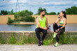 © Georgii - Athletic laughing young couple in stylish sportswear after workout sitting with phone and bottle of water outdoor
