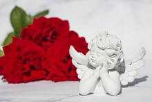 Cute Angel And Red Rose Petals On A White Marble Background. Theme Of Love. Valentine's Day. Postcard For The Holidays.