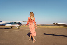 Back View Fashionable Women In Beautiful Classy Pink Dress Walking To A Private Plane And Blue Sky In Background
