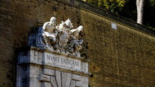 Vatican Museums Written In Italian At The External Entrance Of The Museums On The Vatican Walls, With A Group Of Marble Statues And Papal Coat Of Arms, Seen From The Street