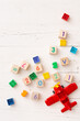 © goodmoments - Developing multi-colored cubes on a white wooden table. Wooden cubes with numbers 2021 and others. Top view of the numbers of the year, a red plane and other educational toys.