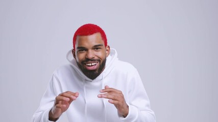 Wall Mural - Worried joyful young bearded african american man with red hair in streetwear hoodie isolated on white color background studio. People lifestyle concept. Looking camera doing winner gesture screaming