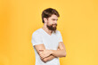 © SHOTPRIME STUDIO - Bearded man in a white T-shirt gestures with his hands emotions studio yellow background